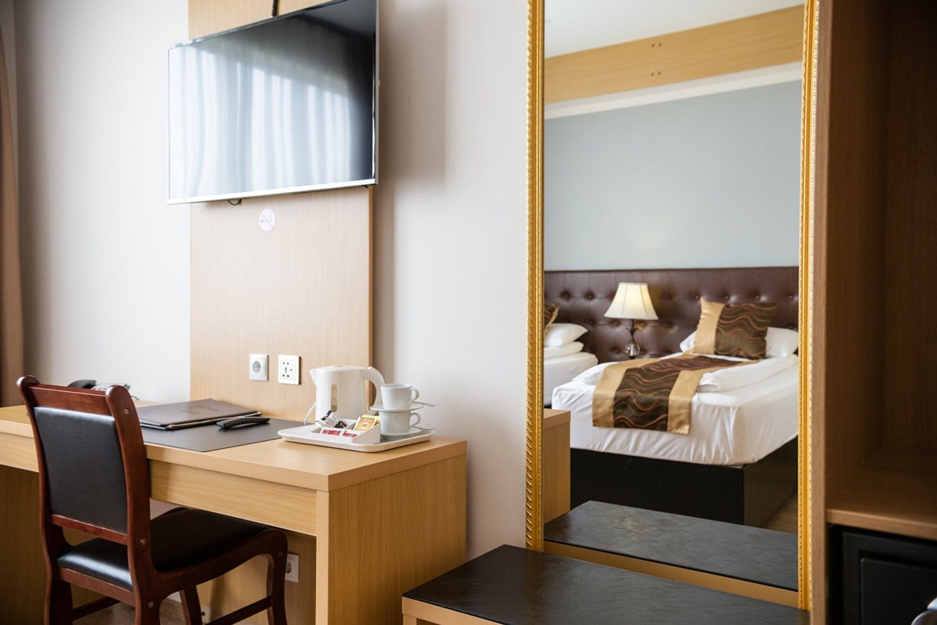 Desk and TV beside a tall gilded mirror reflecting the bed