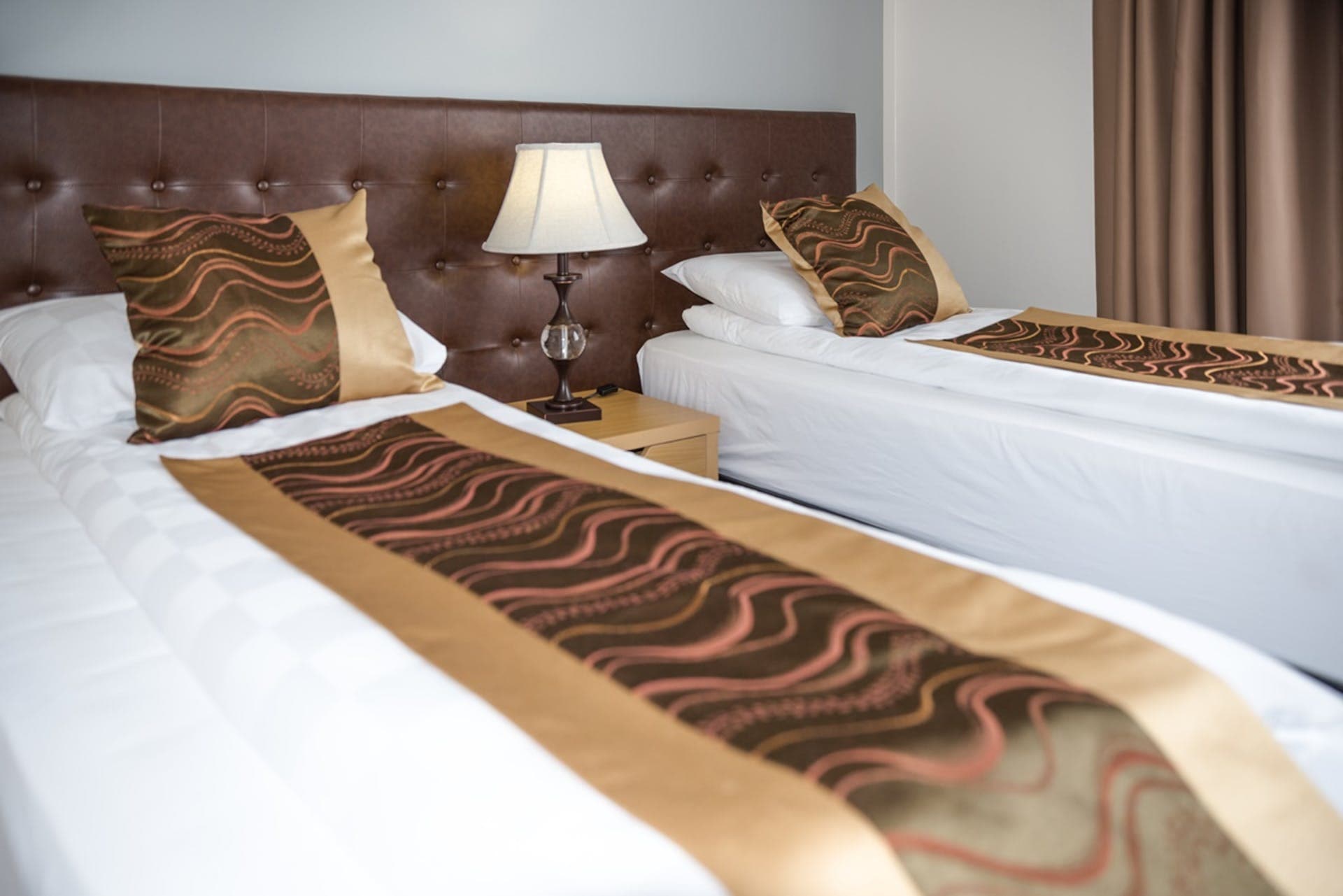 Beds made up with gold and brown runners under a padded headboard