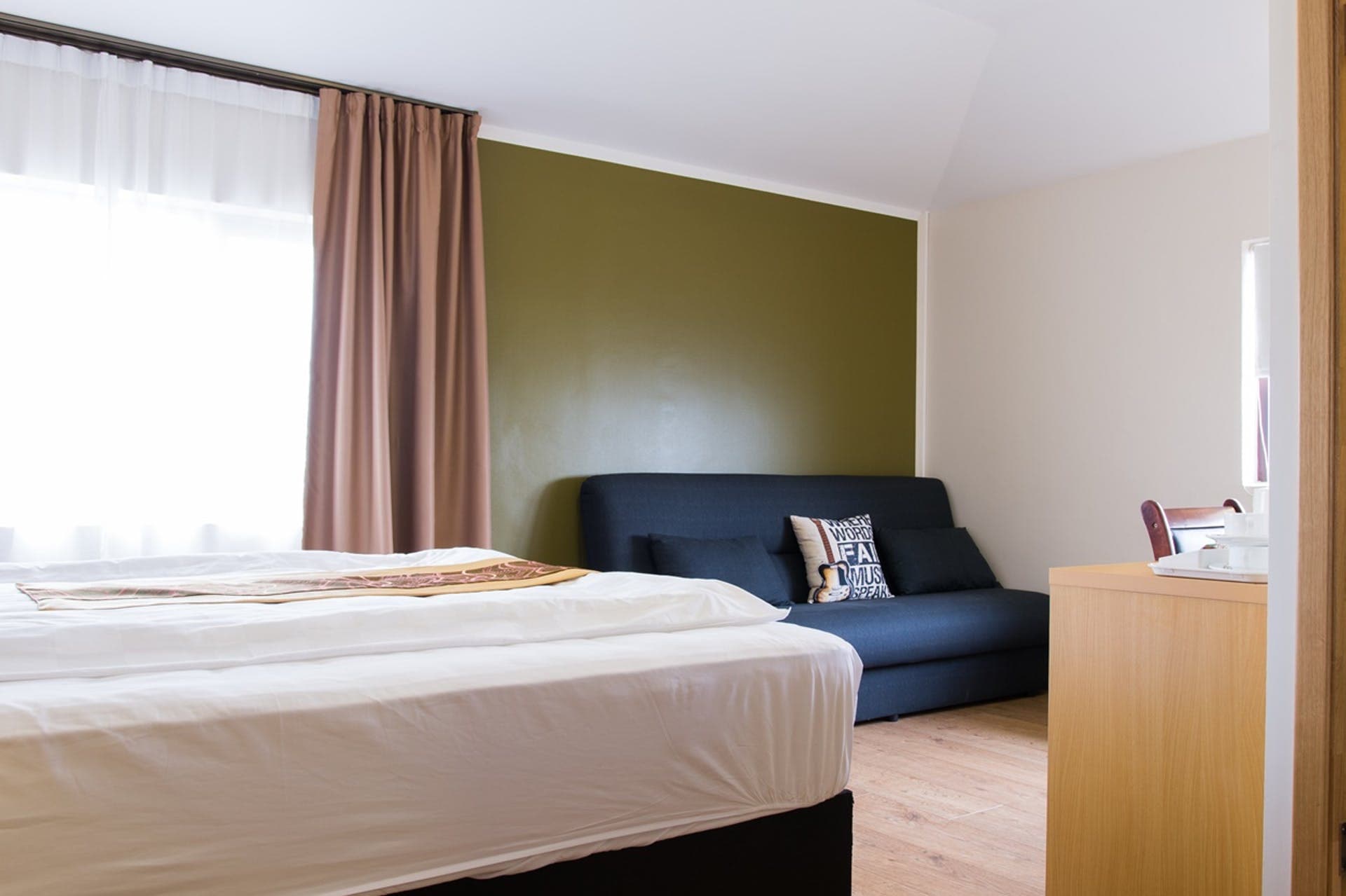 Bed and a navy sofa against an olive green wall