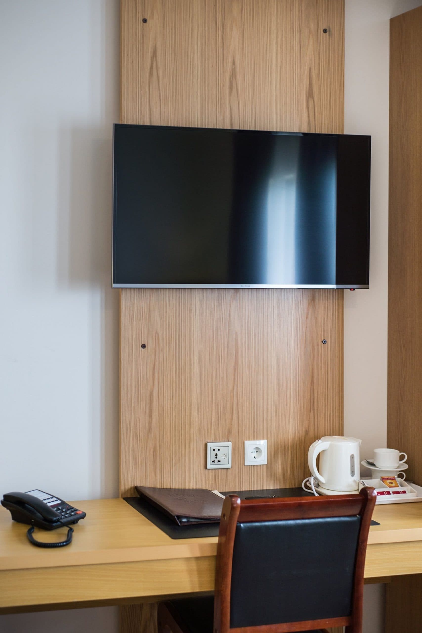Wall mounted TV above a desk with a kettle and a phone