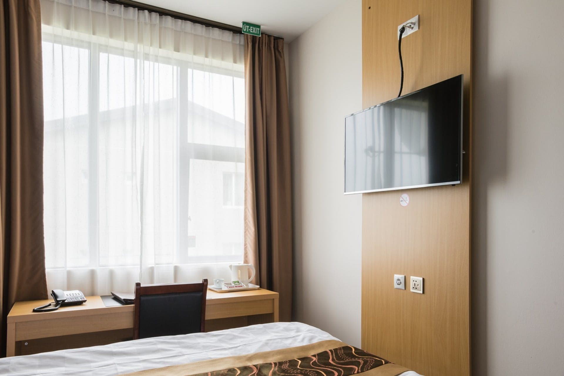 Single bed by the window, with a desk, a phone and a wall mounted TV
