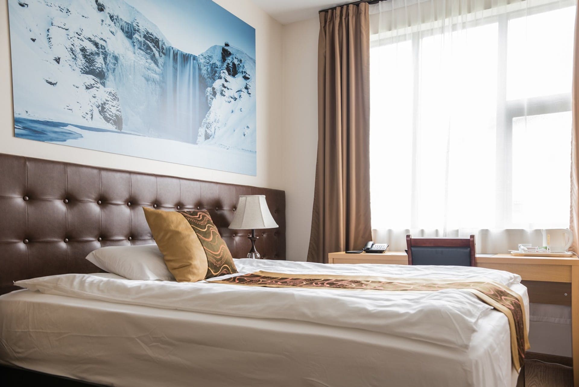 Single room with a padded headboard and a print of a frozen waterfall