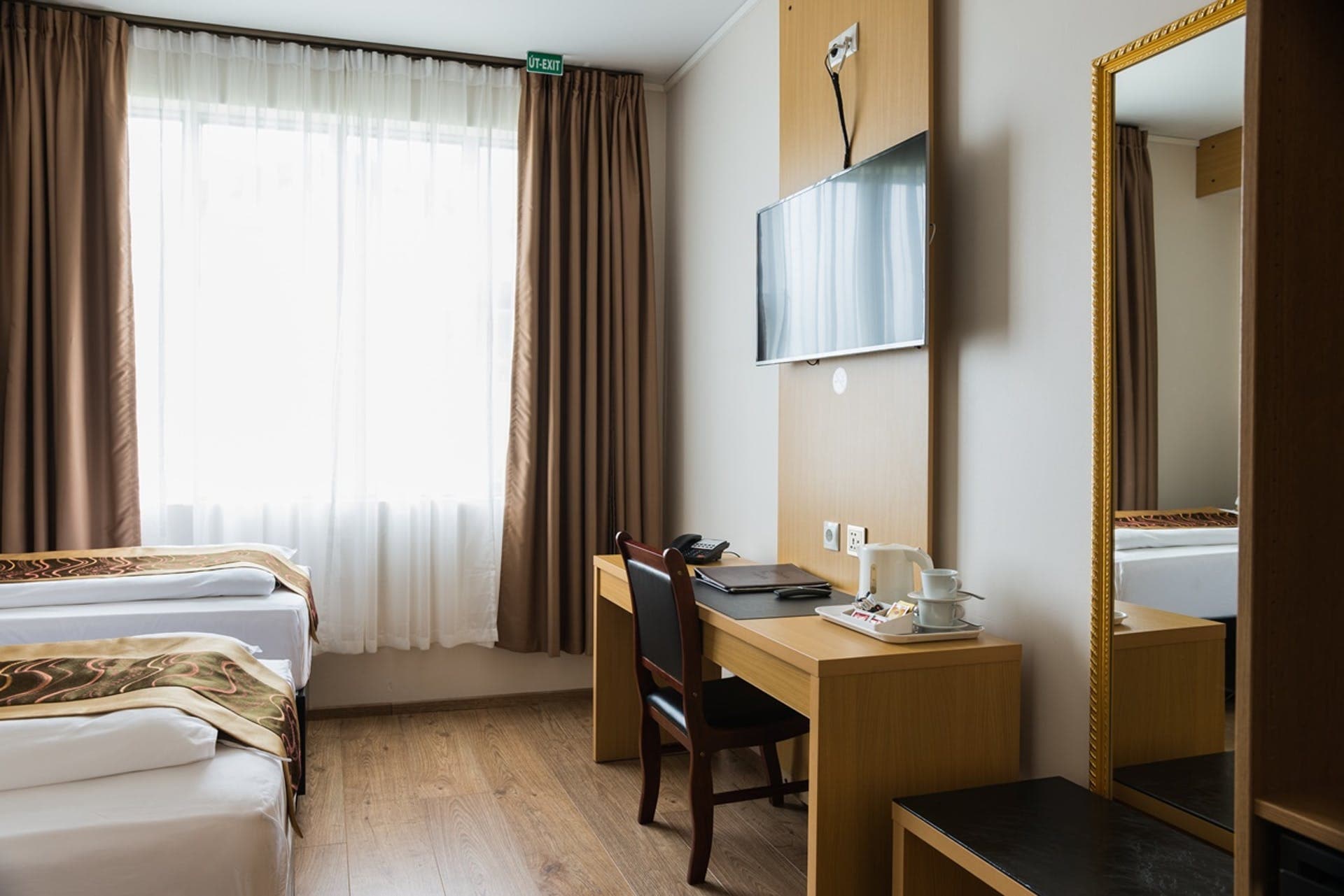 Twin room with a desk, a TV and a tall gilded mirror