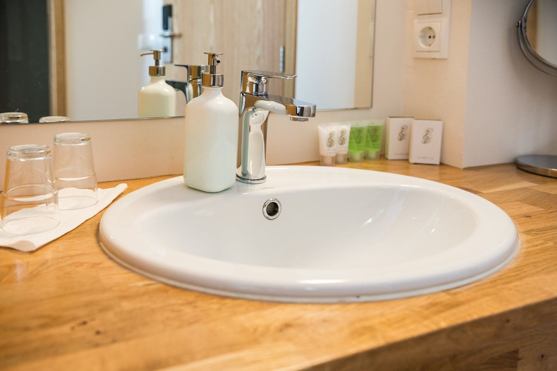 Washbasin on a wooden counter with glasses and toiletries